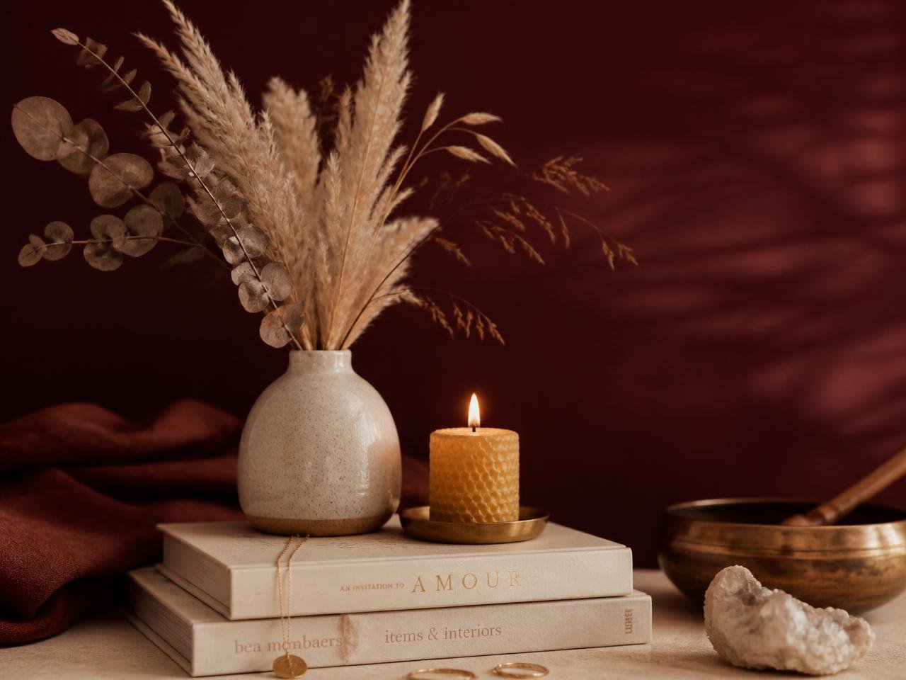 Vaso com flores secas, vela acesa e livros em tons de vinho e areia